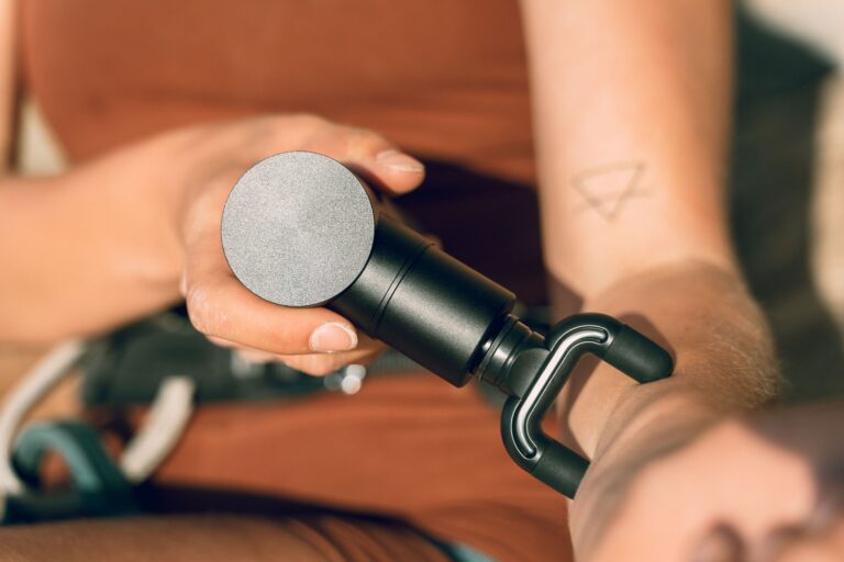 A person sliding their hand into an electric air compression hand massager with an active LED display panel on a desk.